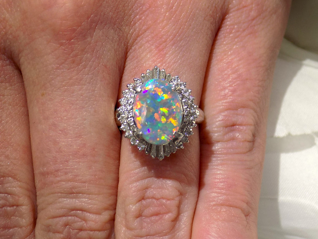 This is a women's ring with 2.51ct lightning ridge natural opal surrounded by .72ct natural baguette and round diamonds in 14K white gold on a women's finger with a white background.