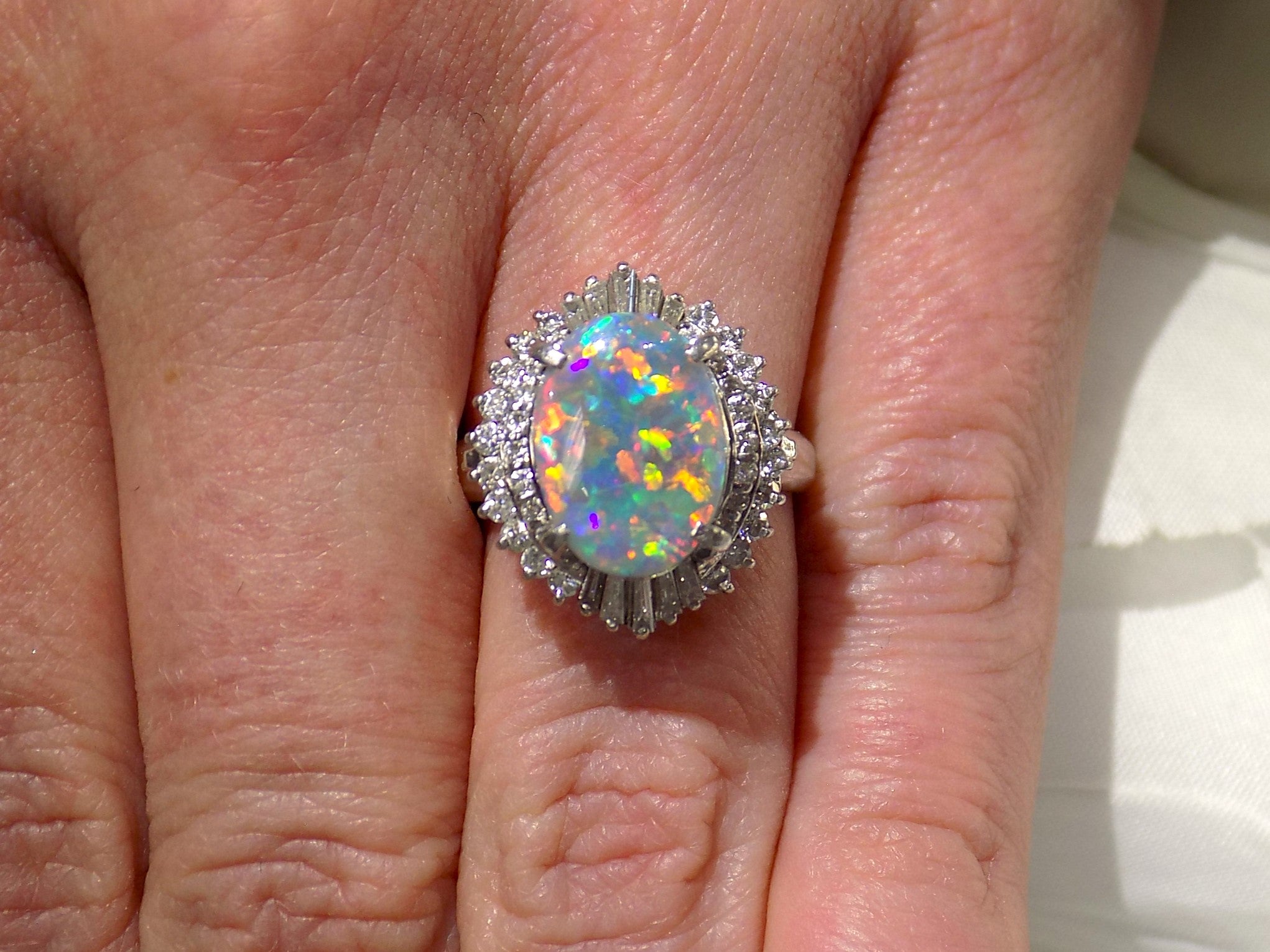 This is a women's ring with 2.51ct lightning ridge natural opal surrounded by .72ct natural baguette and round diamonds in 14K white gold on a women's finger with a white background.