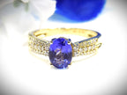 This is a women's natural 1.35ct natural oval tanzanite ring with .36ct natural round diamond accents in 14K yellow gold on a white and blue background.