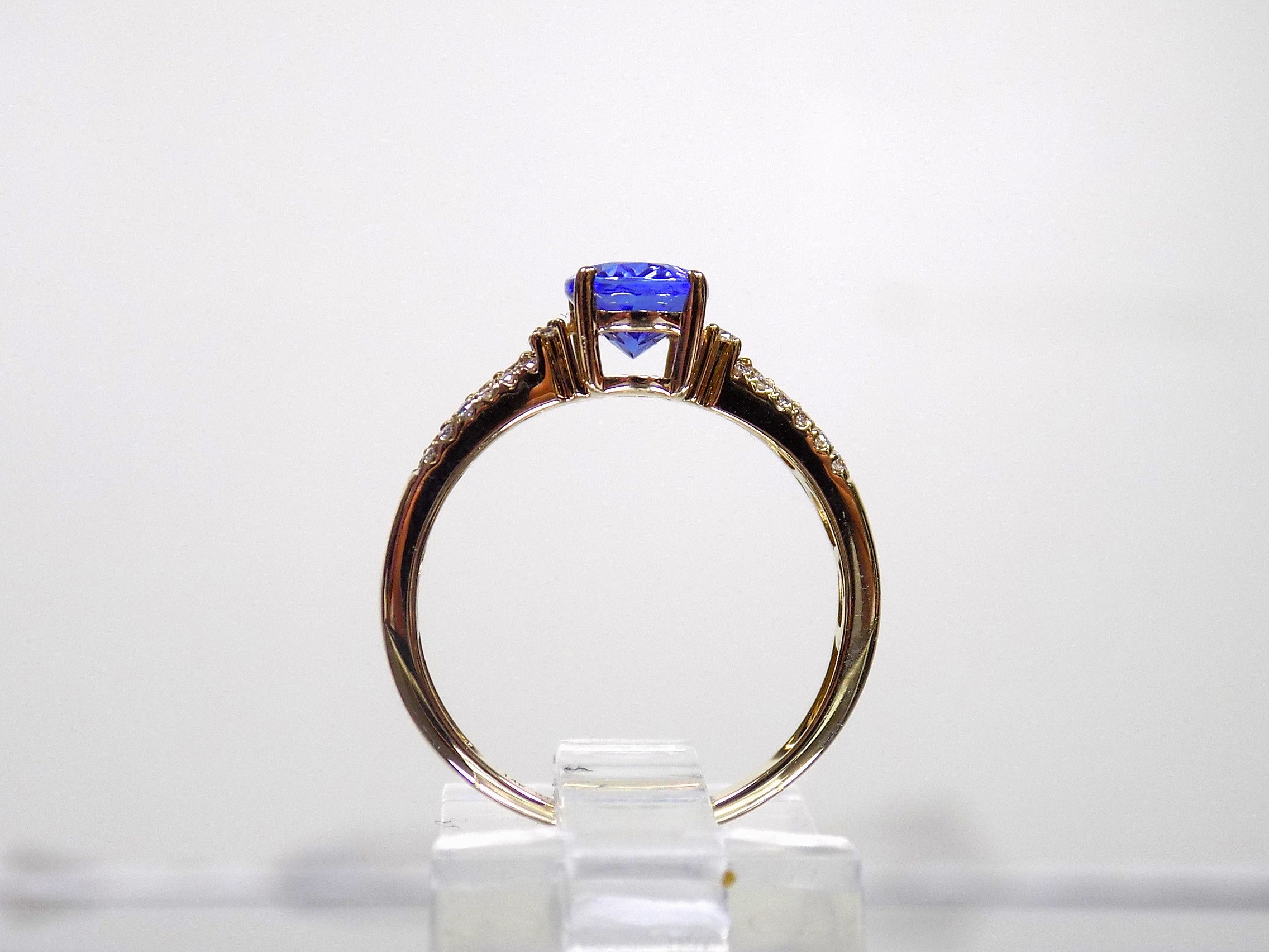 This is a women's natural 1.35ct natural oval tanzanite ring with .36ct natural round diamond accents in 14K yellow gold on a white background from a side view.