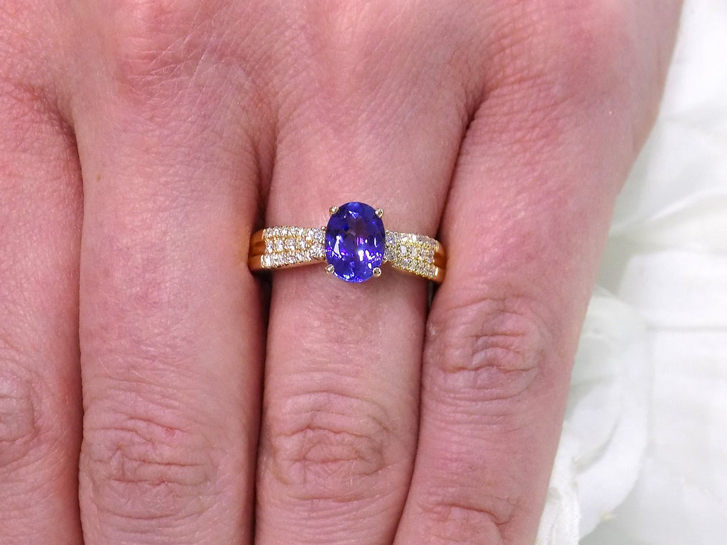 This is a women's natural 1.35ct natural oval tanzanite ring with .36ct natural round diamond accents in 14K yellow gold on a women's finger.