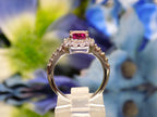 This is a women's ring with a 1.47ct natural emerald cut pink tourmaline surrounded by .67ct natural round diamonds set in 14K white gold on a mirrored surface with a blue floral background from a side view.