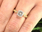 This is a women's natural round brilliant diamond ring with a 1.10ct round center and .22ct in diamond accents set in yellow gold shown on a woman's finger.