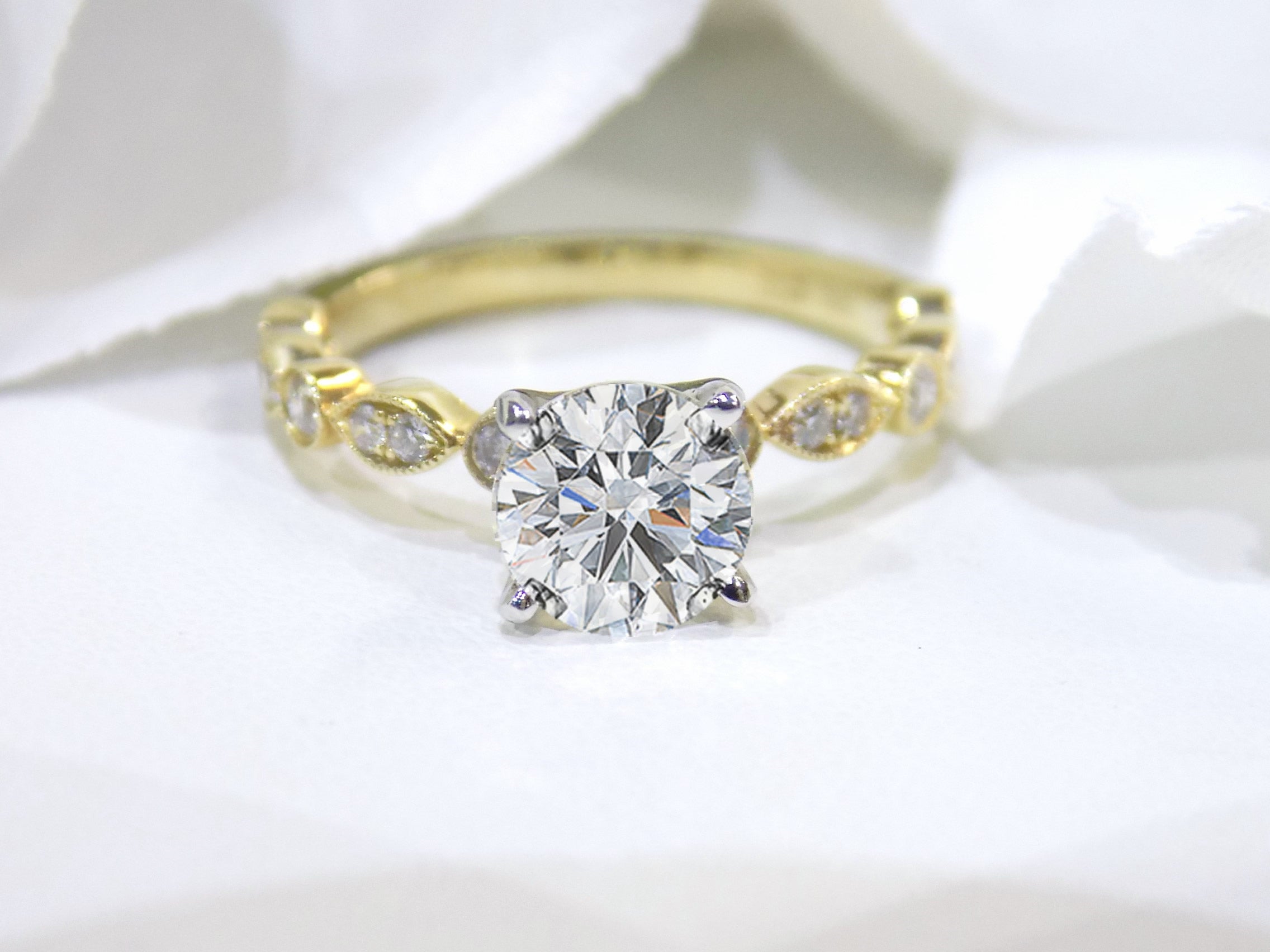 This is a women's natural round brilliant diamond ring with a 1.10ct round center and .22ct in diamond accents set in yellow gold shown with a white background.