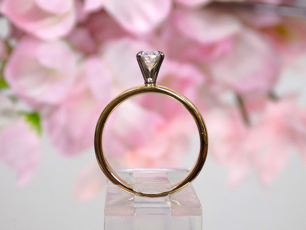 This is a side view of a .45ct natural round brilliant solitaire ring on wider yellow gold band with floral background.