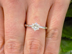 The is a natural .60ct round brilliant diamond solitaire engagement ring in white gold shown on a woman's finger.