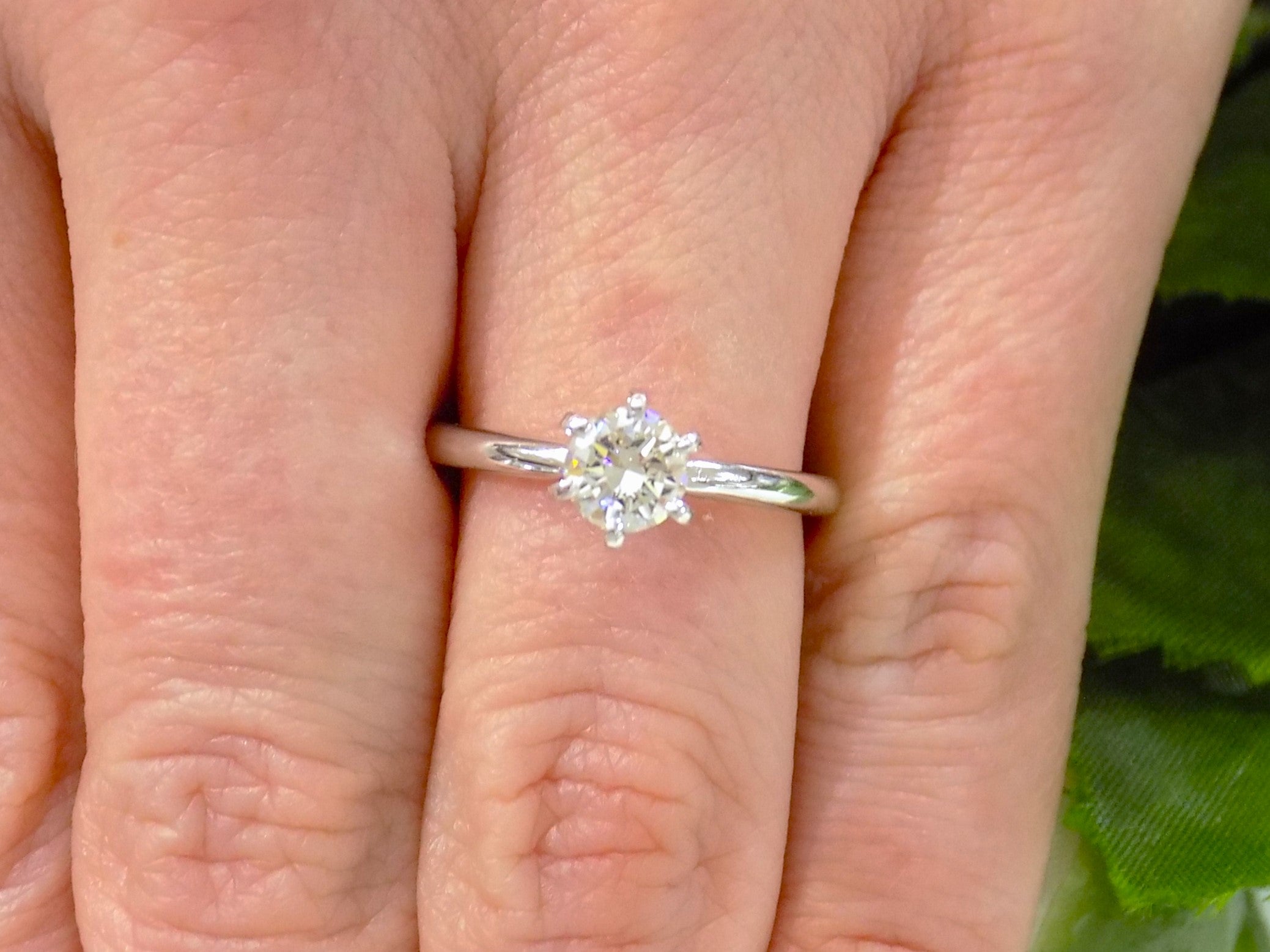 The is a natural .60ct round brilliant diamond solitaire engagement ring in white gold shown on a woman's finger.