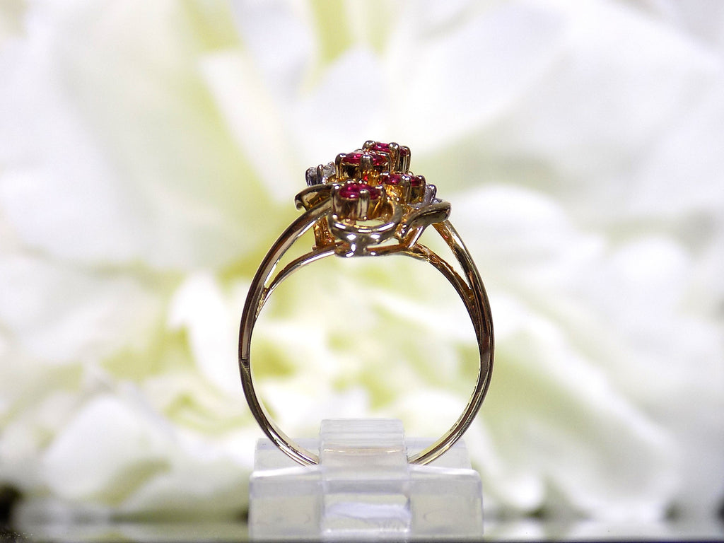 This is a women's .50ct total weight ruby and diamond cluster ring set in 14K yellow gold on a white floral background from a side view.
