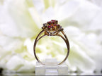 This is a women's .50ct total weight ruby and diamond cluster ring set in 14K yellow gold on a white floral background from a side view.