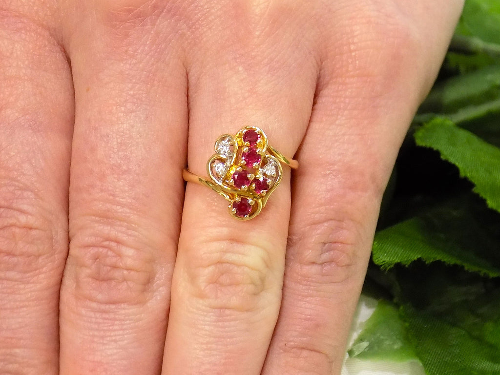 This is a women's .50ct total weight ruby and diamond cluster ring set in 14K yellow gold on a women's ring with a green leafy background.