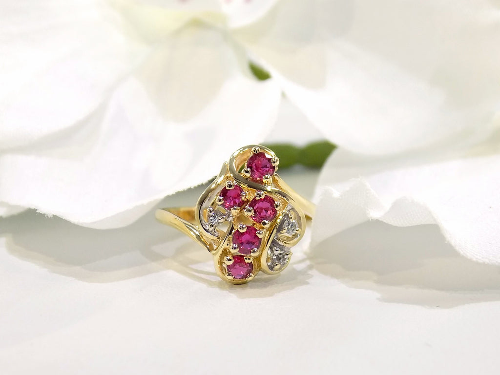 This is a women's .50ct total weight ruby and diamond cluster ring set in 14K yellow gold on a white floral background.