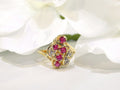 This is a women's .50ct total weight ruby and diamond cluster ring set in 14K yellow gold on a white floral background.