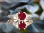 This a 1.51ct total weight natural oval pigeon blood red ruby with a single trillion shaped natural diamond on either side in platinum from our estate collection with a flowery mirrored background. 