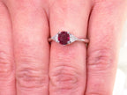 This a 1.51ct total weight natural oval pigeon blood red ruby with a single trillion shaped natural diamond on either side in platinum from our estate collection shown on a woman's finger.