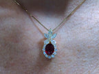 This is a women's 3.06ct total weight oval shape ruby and natural diamond pendant is in yellow gold shown on woman's neck.