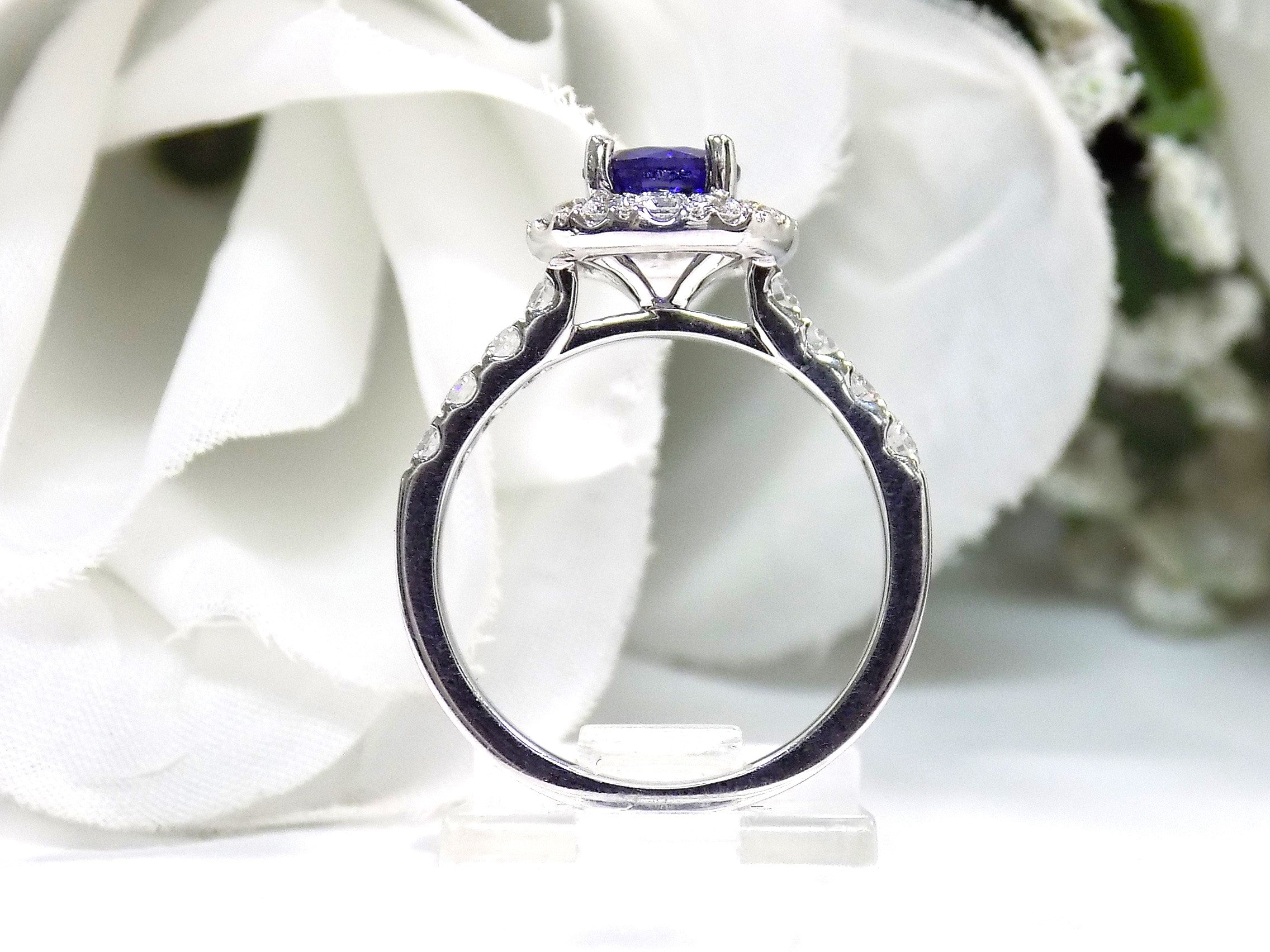 This is a side view of women's halo style 2ct total weight round sapphire and diamond ring in white gold with a white blue background.