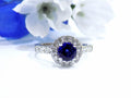 This is a women's halo style 2ct total weight round sapphire and diamond ring in white gold with a white blue background.