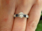 This is a white gold sapphire and diamond ring guard or wrap with an oval solitaire ring in the center shown on a ladies' finger.