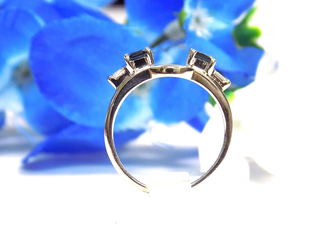 This is a white gold sapphire and diamond ring guard or wrap shown from a side view with blue flower background.
