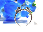 This is a white gold sapphire and diamond ring guard or wrap shown from a side view with blue flower background.