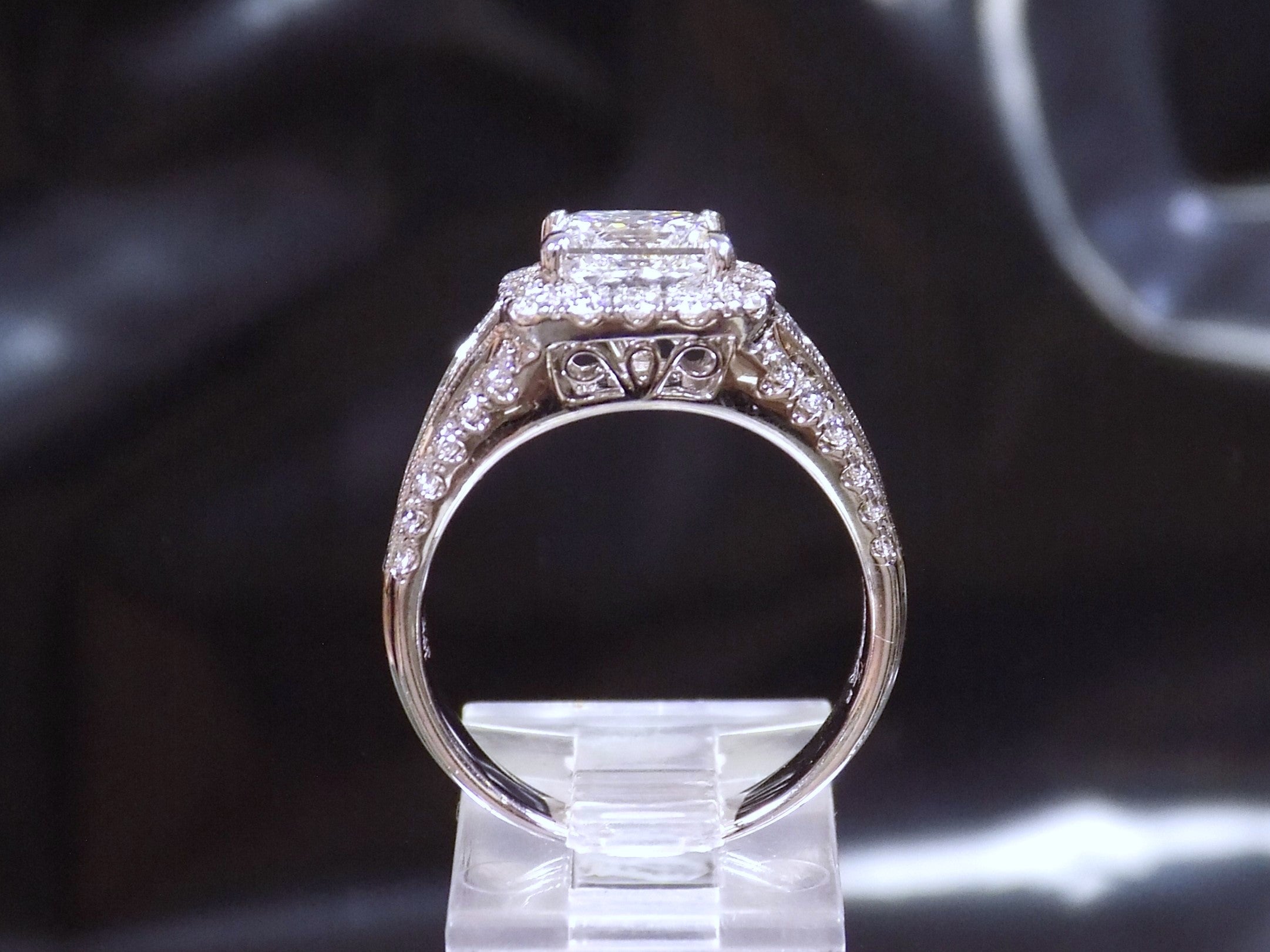 This is a side view of a 3.68ct total weight natural diamond ring with a 2.05ct natural princess cut set in a legendary designer Simon G white gold mounting with a black background.