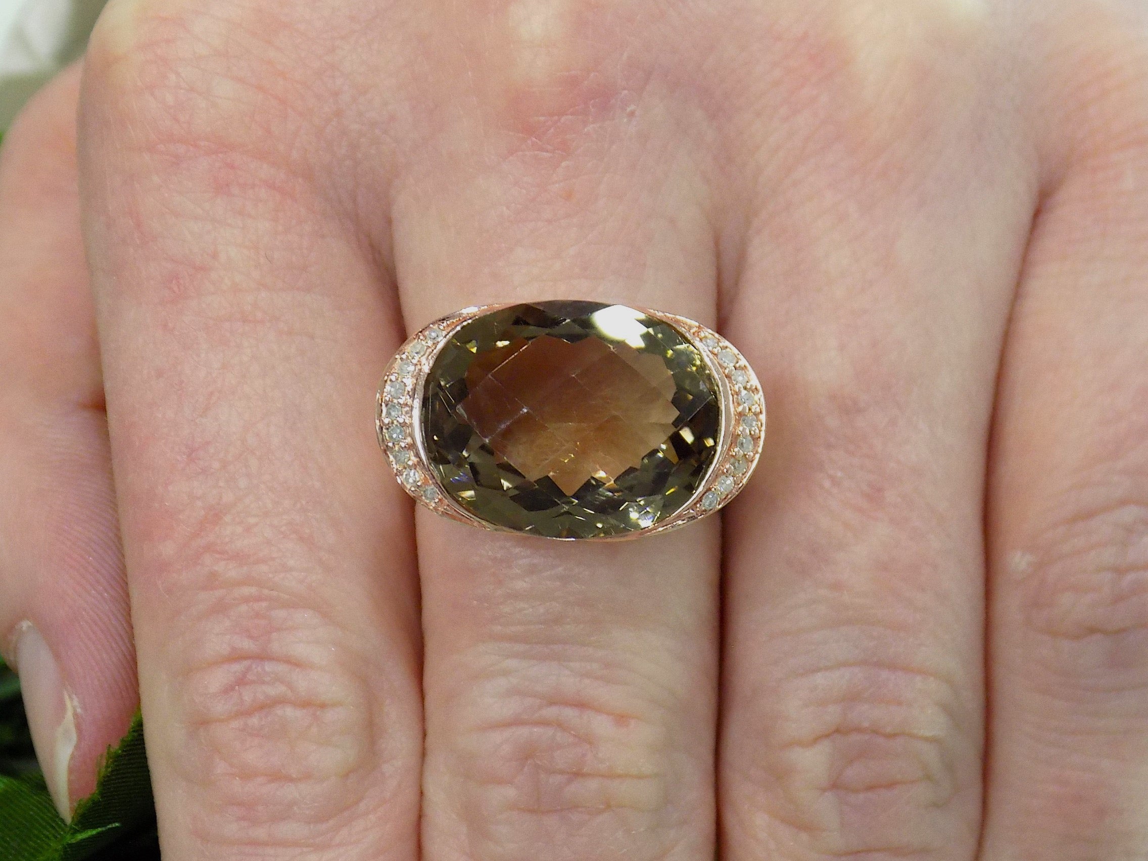 This is a women's ring with a fantasy cut approximate 13ct natural smoky quartz or topaz in the center with .08ct in natural diamonds on both sides set in a filigree style 14K rose gold mounting on a women's finger.