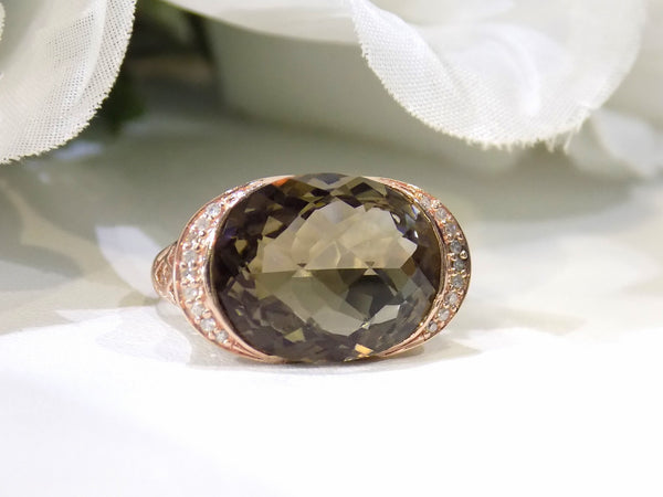 This is a women's ring with a fantasy cut approximate 13ct natural smoky quartz or topaz in the center with .08ct in natural diamonds on both sides set in a filigree style 14K rose gold mounting with a white floral background.