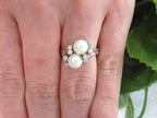 This is a twin cultured pearl ring with natural diamond accents in white gold shown on a ladies' finger.