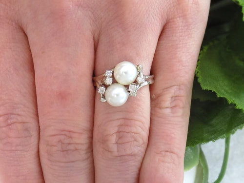 This is a twin cultured pearl ring with natural diamond accents in white gold shown on a ladies' finger.
