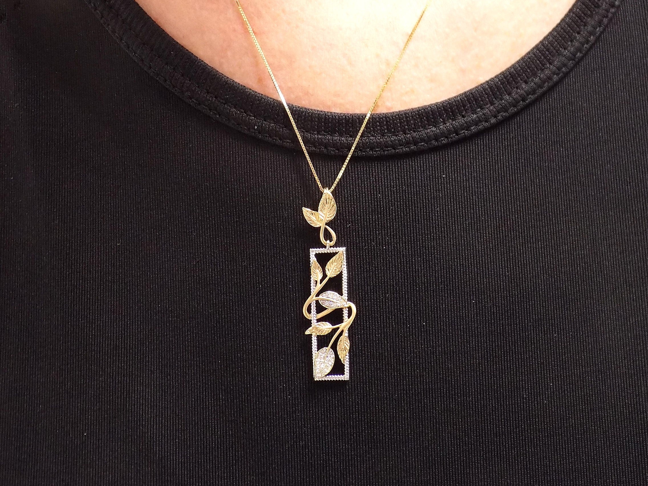 This is a .12ct total weight natural diamond  leaf style looking pendant in two tone 10K white and yellow gold on a ladies neck with a black shirt.