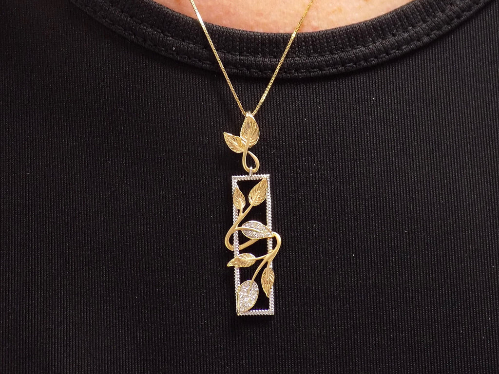This is a .12ct total weight natural diamond  leaf style looking pendant in two tone 10K white and yellow gold on a ladies neck with a black shirt.