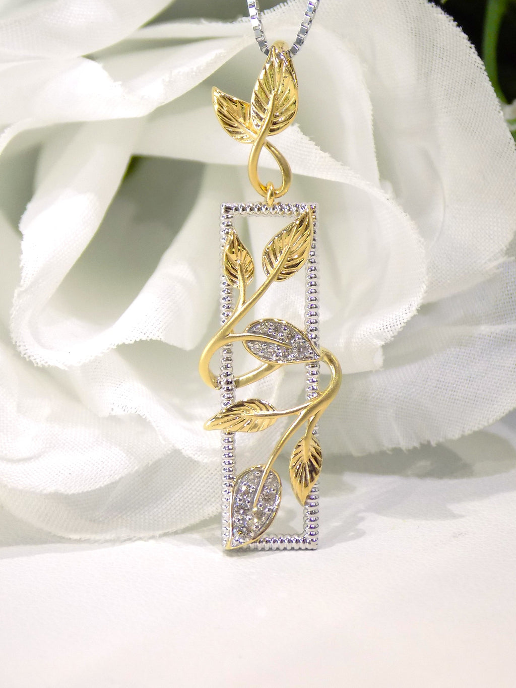 This is a .12ct total weight natural diamond  leaf style looking pendant in two tone 10K white and yellow gold with a white floral background.