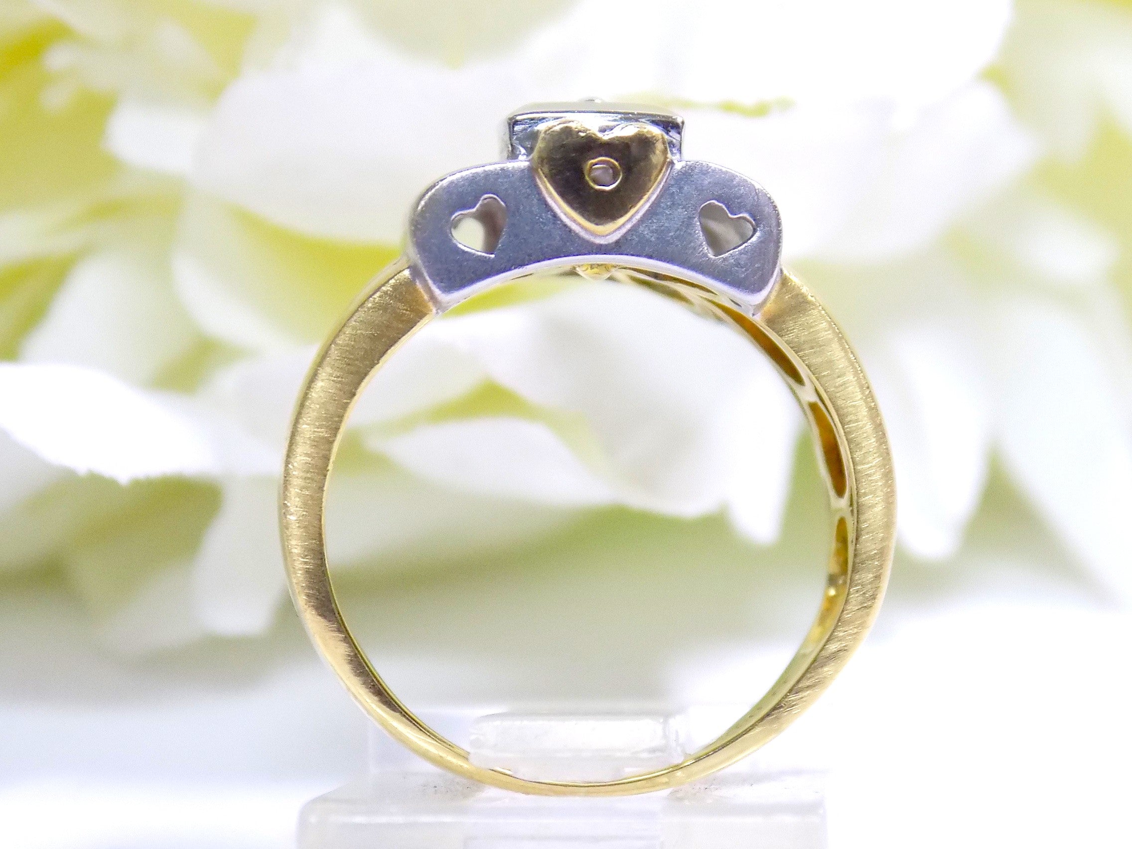 This is a woman's vintage art-deco ring that is two-tone with a brushed 18K yellow and white gold finish with .20ct total diamond weight with a floral background from a side view.