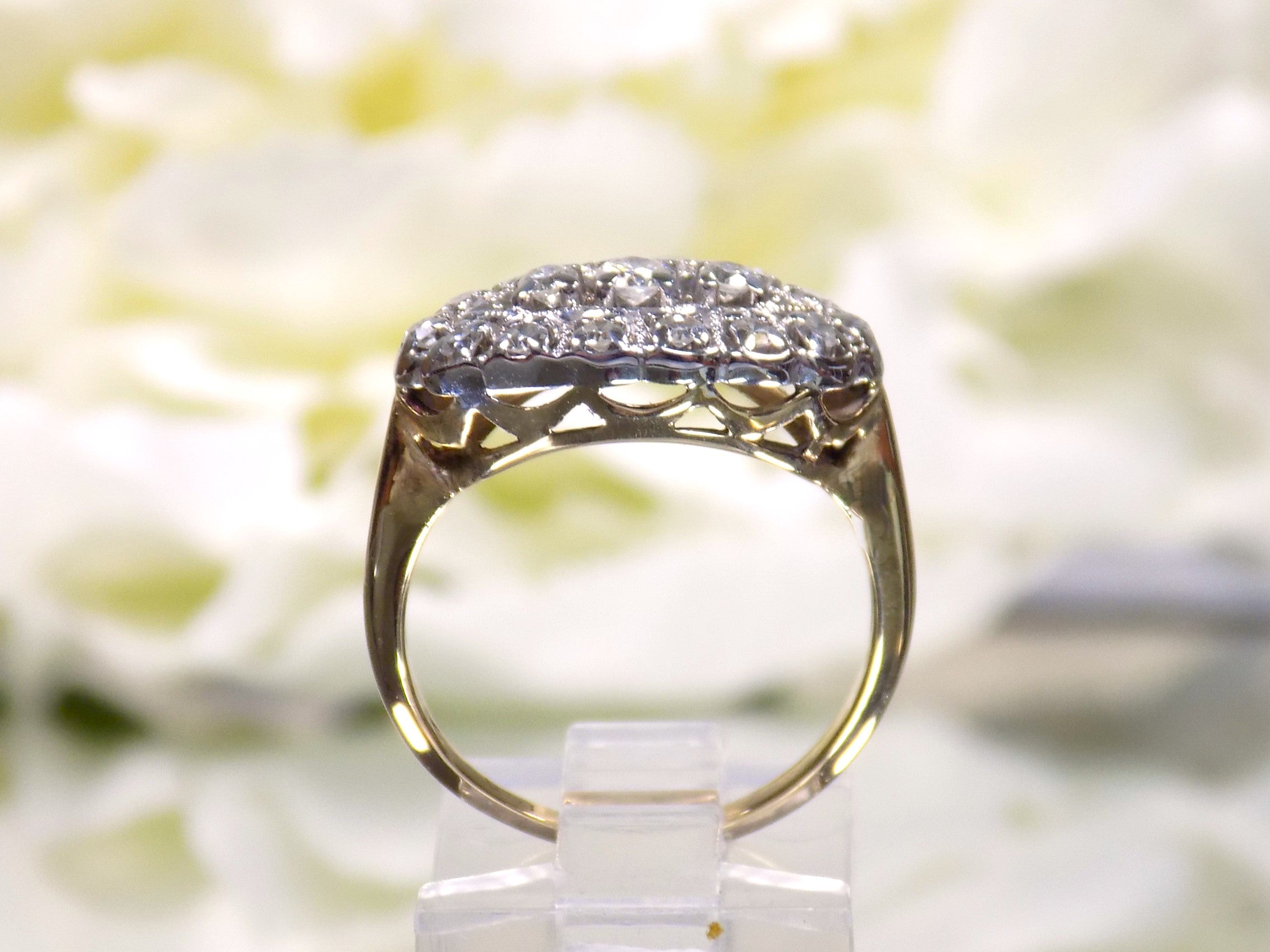 This is a side view of a women's ring called a "princess" style ring usually passed down from mother to daughter throughout the generations.  It a yellow gold ring with diamonds mounted in white gold in the top and has a white flowery background.