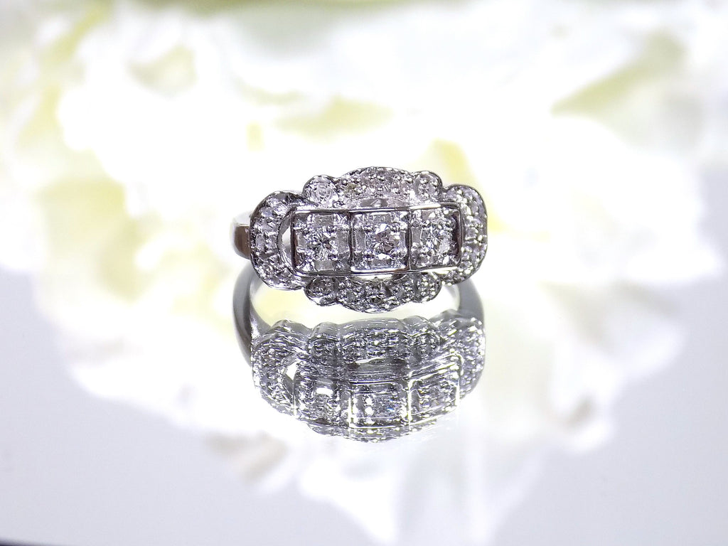 This is a vintage variation of the princess style women's ring with 3 primary diamond in the center with a total weight of .25ct in 14K white gold with a white background.