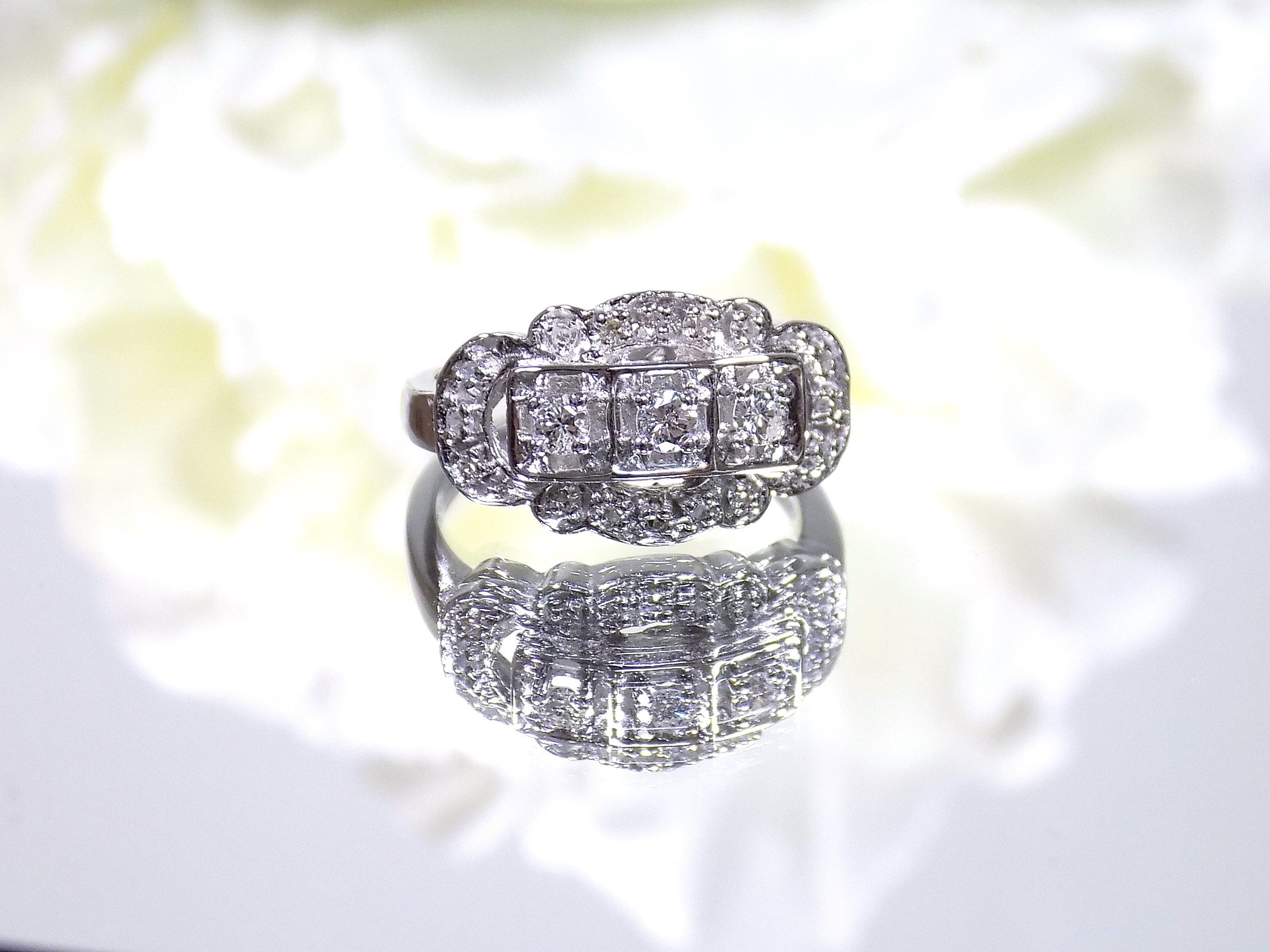 This is a vintage variation of the princess style women's ring with 3 primary diamond in the center with a total weight of .25ct in 14K white gold with a white background.
