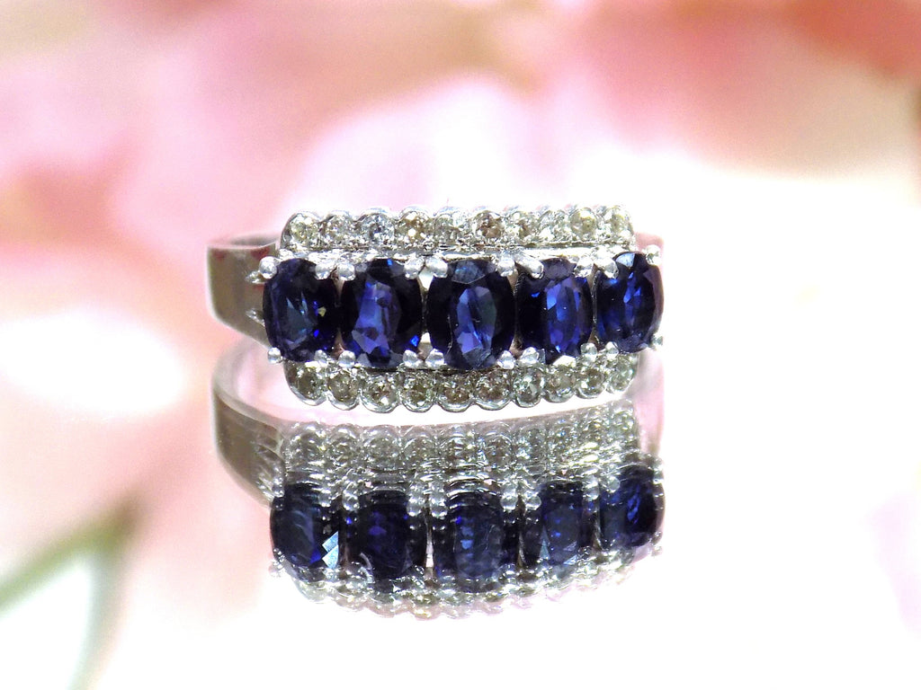 This is a women's vintage estate ring with a total of 2.00ct in natural oval sapphires and round diamonds in 14K white gold on a mirrored surface with a pink floral background.