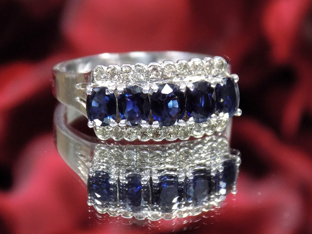 This is a women's vintage estate ring with a total of 2.00ct in natural oval sapphires and round diamonds in 14K white gold on a mirrored surface with a red floral background.
