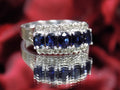 This is a women's vintage estate ring with a total of 2.00ct in natural oval sapphires and round diamonds in 14K white gold on a mirrored surface with a red floral background.