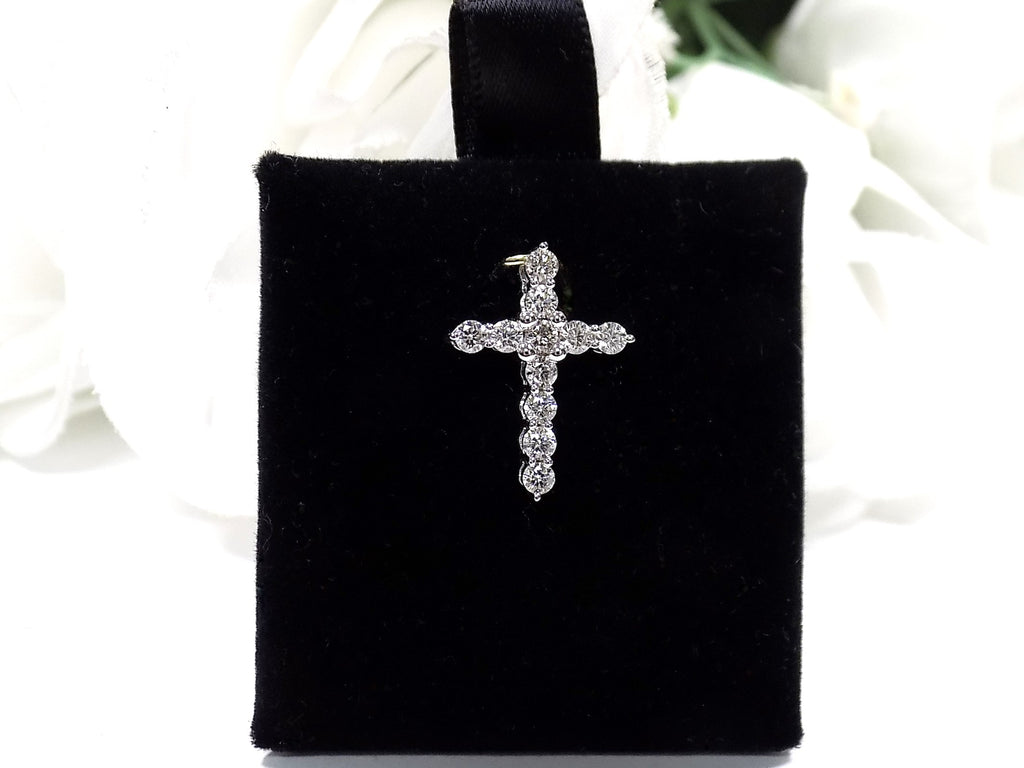 This is a .50ct natural diamond cross pendant in 14K white gold on a black pad with a white floral background.