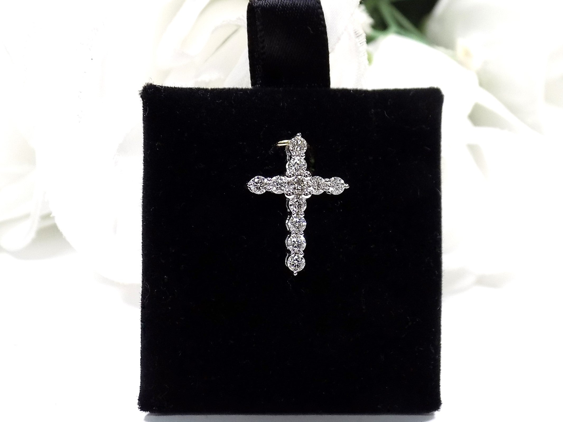 This is a .50ct natural diamond cross pendant in 14K white gold on a black pad with a white floral background.